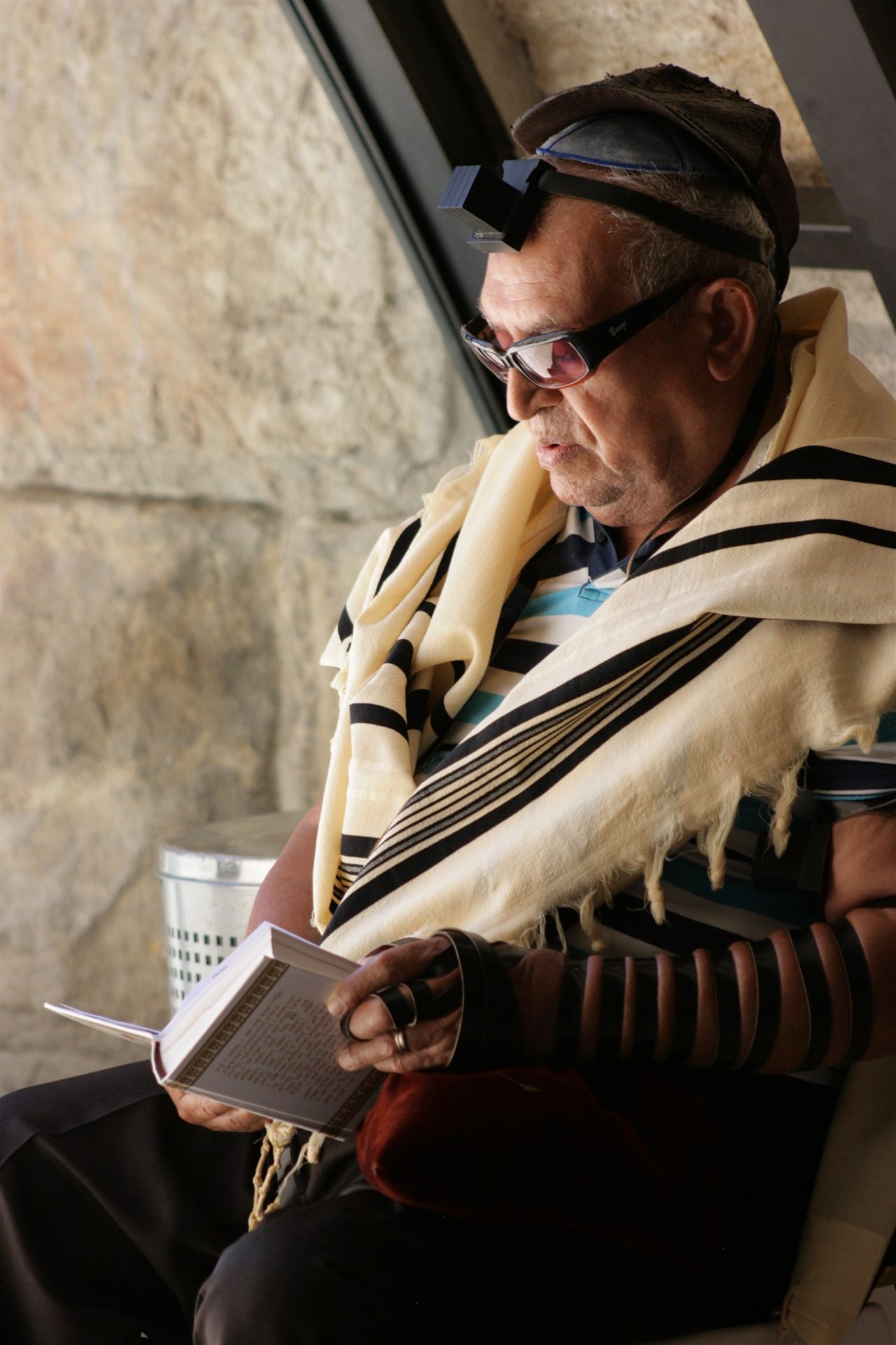 Jewish man wearing tallit and tefillin while reading from a prayer book
