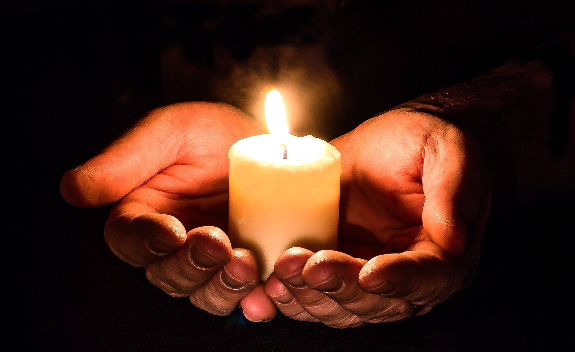 Hands holding a lit memorial candle in darkness